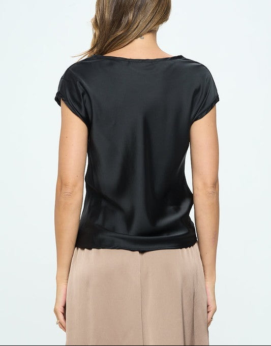 Woman wearing a black satin top and beige pants on a white background