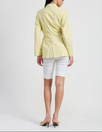 Woman wearing a light yellow blazer and white shorts on a plain background