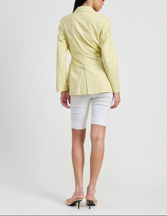 Woman wearing a light yellow blazer and white shorts on a plain background