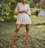 Woman in a grey dress standing in a natural setting with trees and grass.