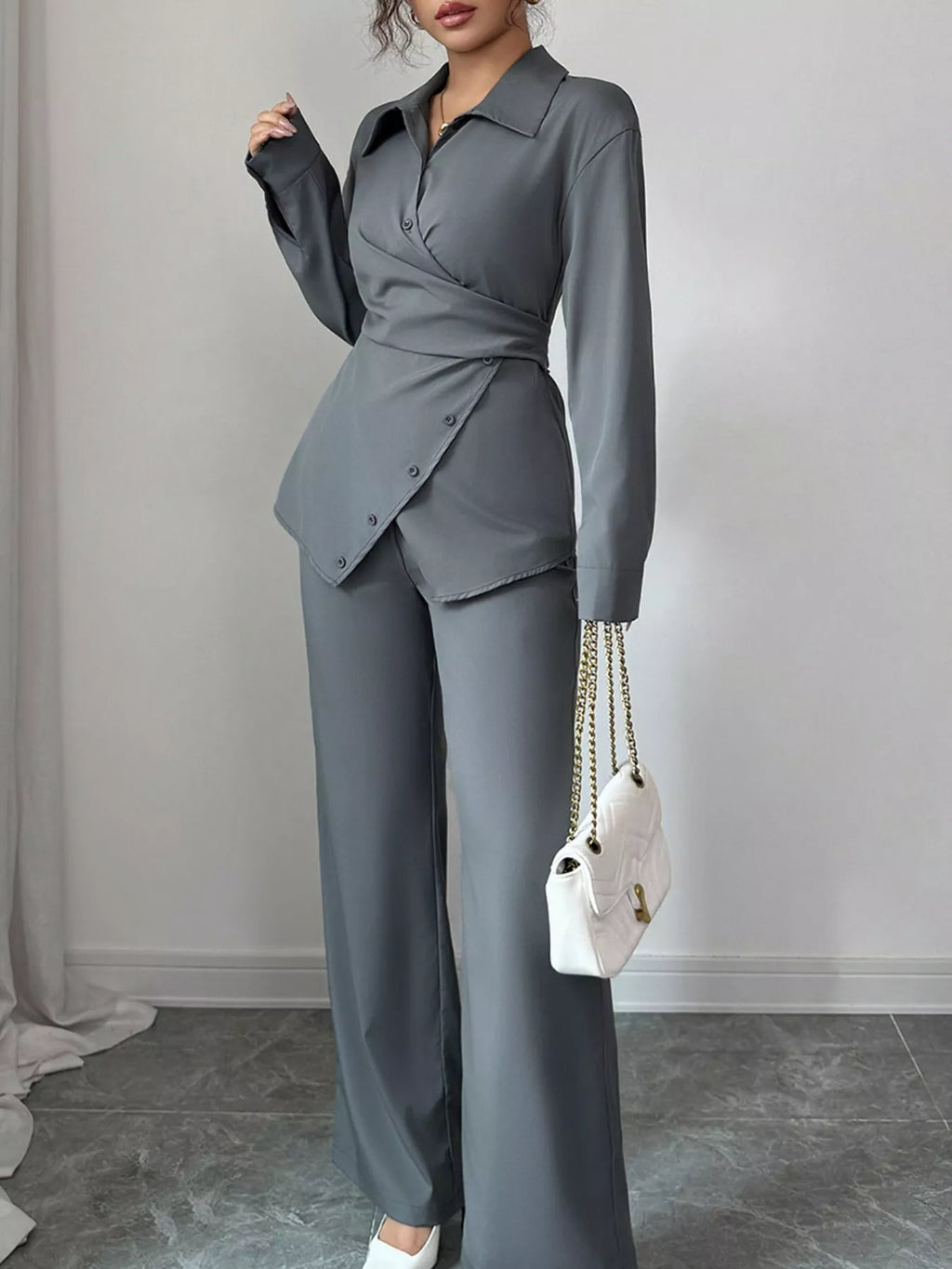 Person wearing a gray suit holding a white handbag against a plain background